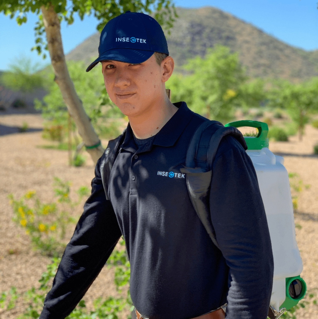 Young Man Wearing a Blue Insectek Hat and Shirt Using a Backpack Sprayer.